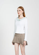 Woman wearing a white long-sleeve top and beige pleated skirt on a white background