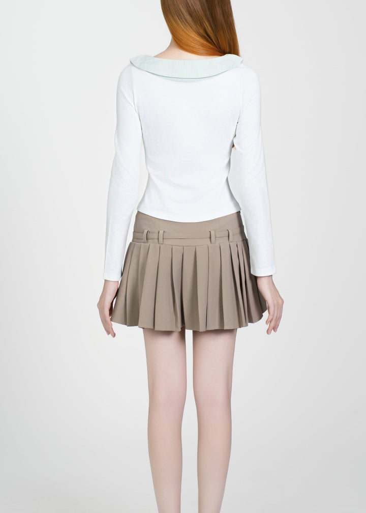Person wearing a white long-sleeve top and beige pleated skirt on a white background