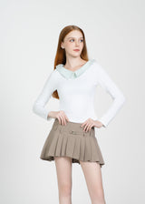 Woman wearing a white long-sleeve top and beige pleated skirt on a white background