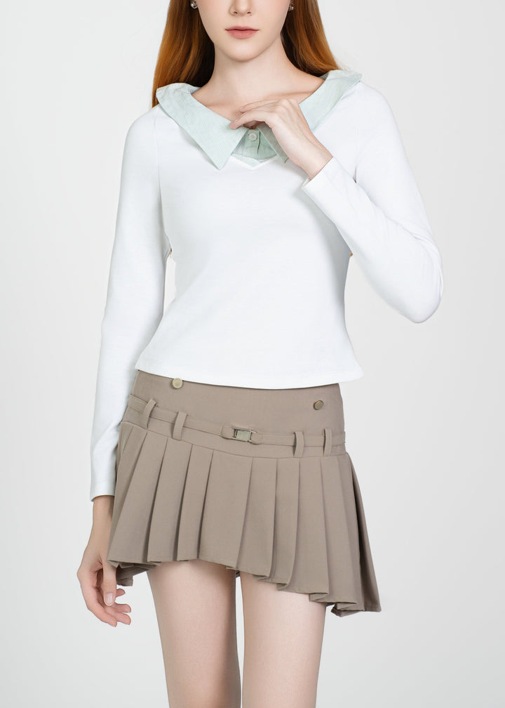 Woman wearing a white long-sleeve top and beige pleated skirt on a white background